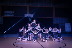 Układ taneczny w wykonaniu dziewcząt w ciemnych błyszczących sukienkach i bolerkach we wzorek Formuły1.