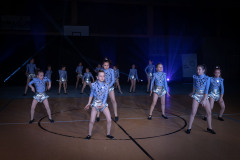 Układ taneczny grupy dziewcząt w srebrnych szortach z falbanką i niebieskich bluzkach ze świecącymi rombami.