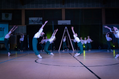 Układ taneczny w wykonaniu dziewcząt w zielonych spodniach i białych koszulach. Na pierwszym planie tancerki wyginające się w tył z wyrzyconymi w górę rękoma.