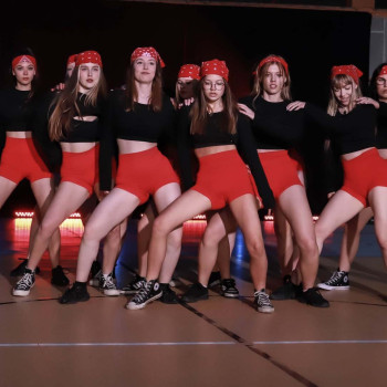 Grupa dziewczyn w układzie tanecznym. Ubrane w czerwone szorty, czarne topy i czerwone bandanki.
