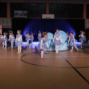 Grupa podczas występu w sali gimnastycznej. Dziewczynki ubrane w biało-niebieskie sukienki.