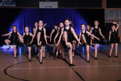 Grupa dziewczynek w czarnych błyszczących sukienkach. Podnoszą w górę prawe nogi.