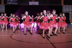 Grupa podczas występu. Dziewczynki ubrane w czerwone tiulowe sukienki z czarnymi wstawkami.