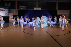 Grupa podczas występu w sali gimnastycznej. Dziewczynki ubrane w biało-niebieskie sukienki.