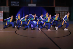 Grupa podczas występu w sali gimnastycznej. Luźne sportowe bluzy i spodnie w niebieskie, białe, zielone i żólte figury, pasy.