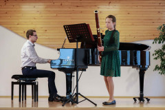 Po prawej dziewczynka grająca na fagocie. Ubrana w zieloną koronkową sukienkę. Po lewej mężczyzna akompaniujący na fortepianie.