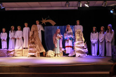 Fragment przedstawienia jasełkowego. Pośrodku sceny Święta Rodzina, a obok w rzędzie stoją aniołowie.