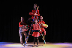 Fragment spektaklu. Metalowa drabina, a na niej cztery dziewczyny w czerwonych strojach z prezentami.