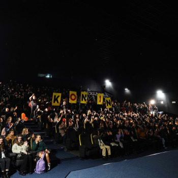 Sala kinowa i siedzący w fotelach tłum wolontariuszy. Między rzędami osoby trzymające żółte plansze z literami układającymi się w napis KONIN.