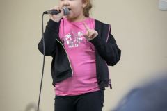 Dziewczynka w czarnym dresie i różowej bluzce śpiewa do mikrofonu.