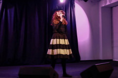 Na scenie dziewczynka z mikrofonem. Ubrama w ciemny włóczkowy beret, czarną bluzkę i spódnicę w białe i czarne pasy.