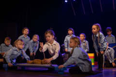 Grupa dzieci na scenie. Pośrodku dziewczynka z igłą zszywa misia.