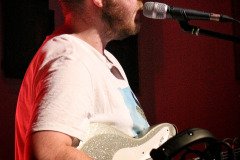 Zdjęcie portretowe. Adam Kempa z gitarą przy mikrofonie.