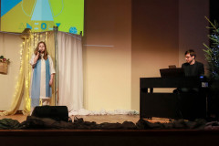 Na scenie dziewczynka w białej sukience i niebieskim szalu. Po prawej akompaniator.
