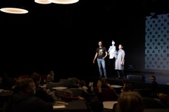 Widownia przy stolikach. Na scenie sali klubowej aktorzy prezentują lalkę.