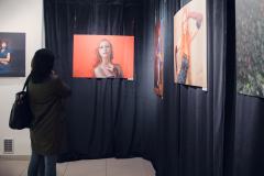 Uczestniczka wystawy ogląda zdjęcie rudowłosej kobiety przedstawionej na czerwonym tle.