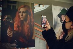 Kobieta fotografuje telefonem zdjęcie przedstawiające rudowłosą dziewczynę. Dziewczyna trzyma w dłoni szklaną kulę, w którą spogląda.
