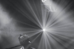 Muzyk grupy Bokka przy klawiszach i mikrofonie. W centrum kadru strumień światła reflektora. Zdjęcie czarno-białe.
