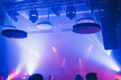 Sala klubowa CKiS. Sylwetki publiczności i sufit z lampami i rusztowaniem oświetlenia. W głębi kadru muzycy na scenie.