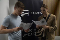 Mężczyzna i kobieta studiują ulotki ElectroNOT. Za nimi baner reklamowy Fortis.