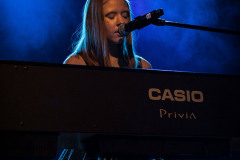 Dziewczyna przy keyboardzie z napisem Casio Privia. Śpiewa do mikrofou na statywie.
