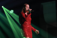Na scenie dziewczyna w czerwonej cekinowej sukience. Za plecami snopy zielonego światła. Zdjęcie w planie amerykańskim.
