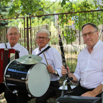 Trzech panów z zespołu siedzi i pozuje do zdjęcia. Od lewej: akordeonista, bębniarz i klarnecista.