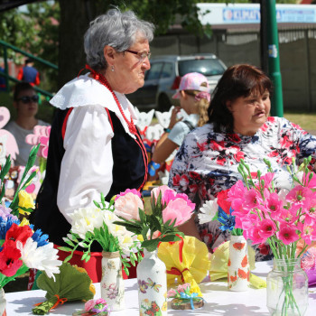 Na stole barwne kwiaty wykonane z bibuły. Oglądają je dwie kobiety.