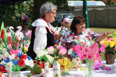 Na stole barwne kwiaty wykonane z bibuły. Oglądają je dwie kobiety.