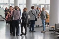Grupa kobiet w trakcie rozmowy w foyer CKiS-DK Oskard. W głębi kadru trzy białe filary oraz schody.