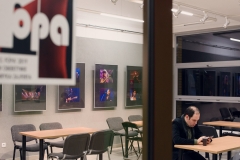 Sala MGOK w Ślesinie. Na ścianei reprodukcje fotografii muzyków. W lewym górnym rogu rozmyty plakat FOPA. W prawym dolnym rogu mężczyzna przy plastikowym kubku z telefonem w dłoni.