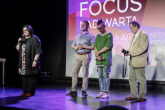 Po lewej Renata Rudowicz z mikrofonem. Obok kolejno stoją jurorzy: Patryk Koszela, Damian Drewniak i Mirosław Jurgielewicz. Za nimi slajd z napisem Focus nad Wartą.