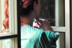 Portret kobiety w zielonej sukience stojącej przy otwartym oknie. Odwrócona plecami do obiiektywu. Autor: Jan Witkowski.