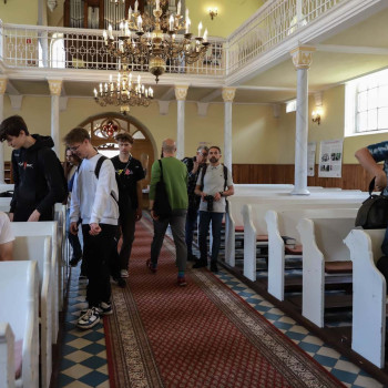 Uczestnicy spaceru zajmują miejsca w ławkach w kościele ewangelicko-augsburskim.