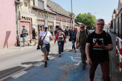 Uczestnicy spaceru idą ulicą Ubranowskiej. Wkraczają na pomalowane na niebiesko miejsce parkingowe dla osoby niepełnosprawnej.