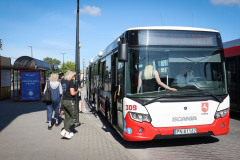 Czerwono-biały autobus MZK z wyświetlonym napisem Focus nad Wartą. Przy kierowcy odwrócona plecami blondynka. Kilka osób stoi przy autobusie. W głębi przystanek z napisem Psychologia Prawo.