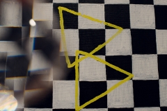 Obraz przedstawiający biało-czarną kratę z dwoma nachodzącymi na siebie  żółtymi trójkątami.