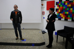 Na podwyższeniu stoi Robert Brzęcki. Lewa stopa na niebieskim kwadracie naklejonym na podłodze. Za nim biały ekran. Po prawej Rafaela Jesionowicz.