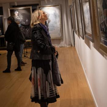 Krystyna Ruminkiewicz ubrana w długą wzorzystą spódnicę i ciemną kurtkę ogląda jedną z prac.