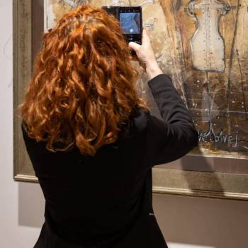 Odwrócona plecami rudowłosa kobieta w czarnym żakiecie robi telefonem zdjęcie jednej z  prac, przedstawiającej manekiny krawieckie. Kto pracuje w CKiS wie, że to Daria Mach.