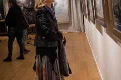 Krystyna Ruminkiewicz ubrana w długą wzorzystą spódnicę i ciemną kurtkę ogląda jedną z prac.