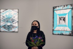 Iza Kostiukow z bukietem kwiatów w dłoni na tle swoich prac