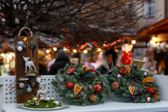 Zbliżenie na świąteczne ozdoby weksponowane na stoisku: dwa wianki, stroik i deska z owieczką.