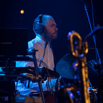 Perkusista ze słuchawkami na uszach przy instrumencie. Sfotografowany z prawego profilu.