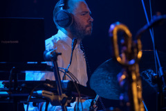 Perkusista ze słuchawkami na uszach przy instrumencie. Sfotografowany z prawego profilu.