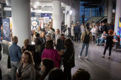 Publiczność podczas rozmów w foyer CKiS-DK Oskard. W tle wiszące plakaty, białe filary i schody wiodące do sali widowiskowej.