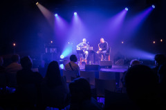 Dariusz Herbasz i Leszek Dranicki na scenie sali klubowej. Niebieskie światła reflektorów. Przed sceną rzędy publiczności.