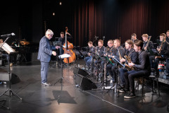 W planie ogólnym na scenie siedzący w trzech rzędach Big Band i dyrygent Krzysztof Pydyński. W głębi pianista i kontrabasista.