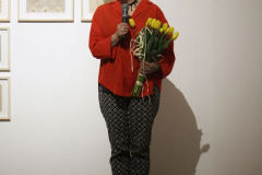 Joanna Imielska mówi do mikrofonu trzymanego w prawej dłoni. W lewej ma bukiet żółtych tulipanów.