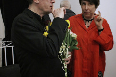 Chwila rozmowy. Sfotografowany z prawego profilu Robert Brzęcki unosi prawą dłoń do ust, w lewej trzyma bukiet. Obok niego Joanna Imielska w czerwieni. Unosi w górę lewą dłoń z wysuniętym w górę placem wskazującym.